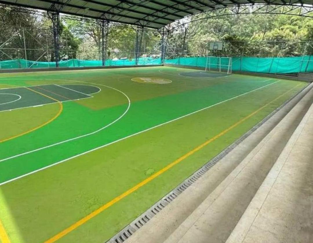 Placa polideportiva con demarcación y pintura en tonos de verde, gradería en concreto, estructura metálica e integrados deportivos